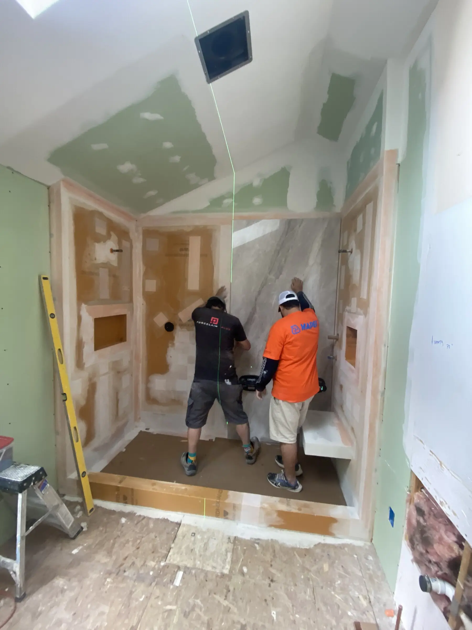 Two Benchmark tile setters installing book-matched porcelain slab walls in a walk-in shower