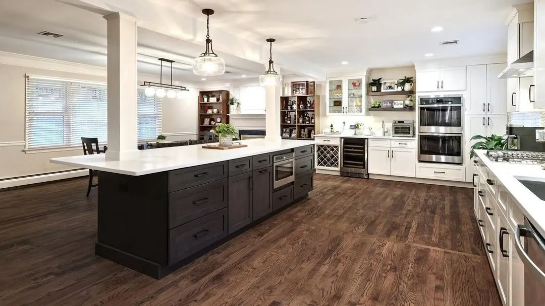 A completed kitchen remodel with a dark shaker island, white perimeter cabinetry, and hardwood floors
