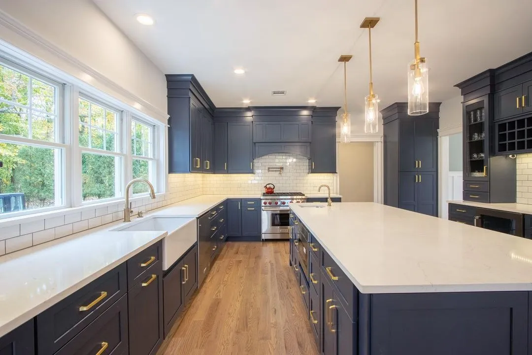 Navy-blue kitchen remodel with a large quartz-topped island, brass hardware, and a white subway tile backsplash, by Benchmark Home Improvements on the New Hampshire Seacoast