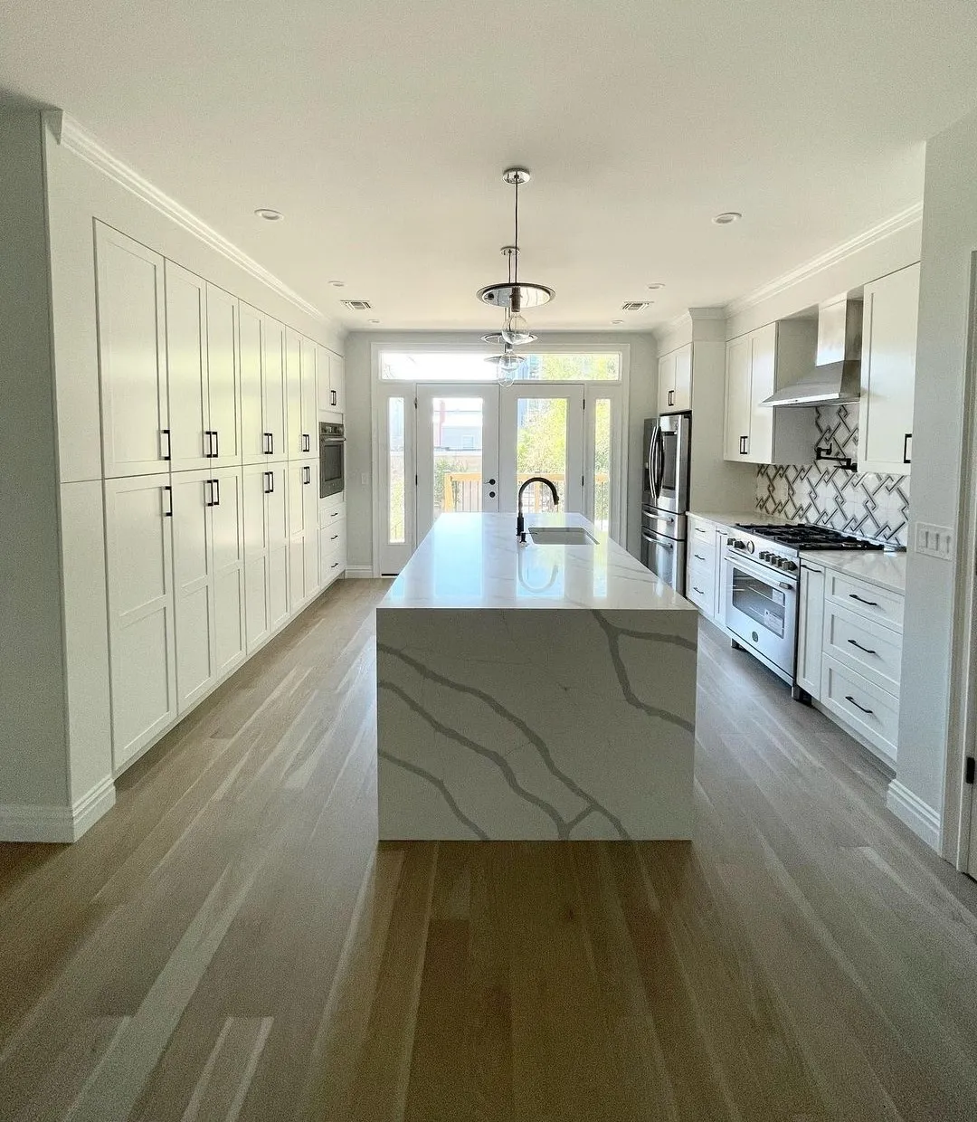 White kitchen with a calacatta quartz waterfall island and professional gas range, remodeled by Benchmark on the New Hampshire Seacoast