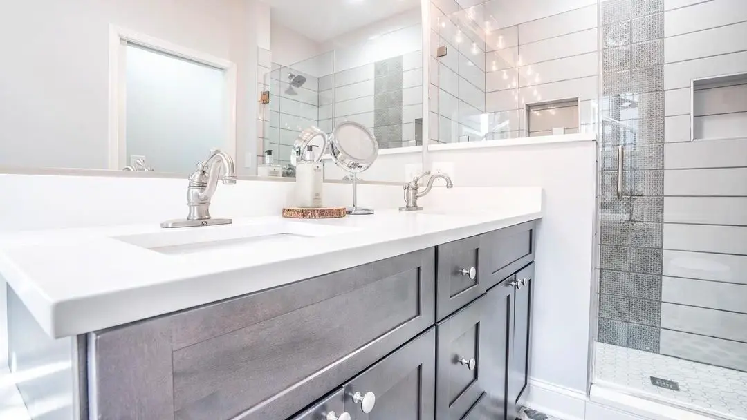 A compact bathroom with a grey vanity, white quartz, and a walk-in glass shower, remodeled by Benchmark on the New Hampshire Seacoast